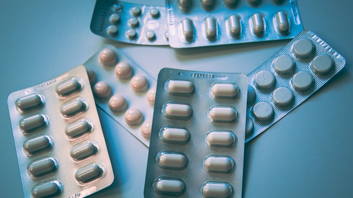 नीली सतह पर सफ़ेद और गुलाबी tablets के कई बिना brand वाले blister packs