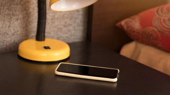 A phone on a bedside table beside a lamp