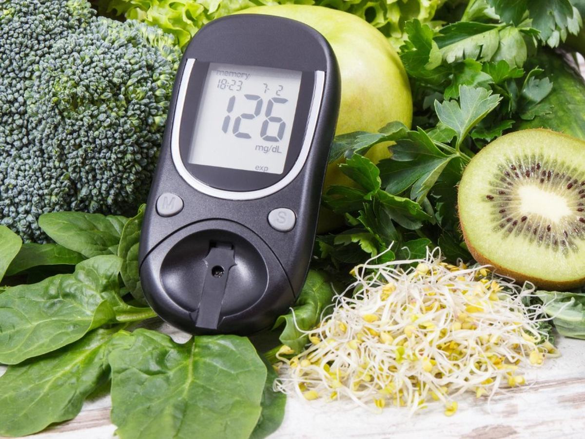 A glucometer beside greens, kiwi and sprouts
