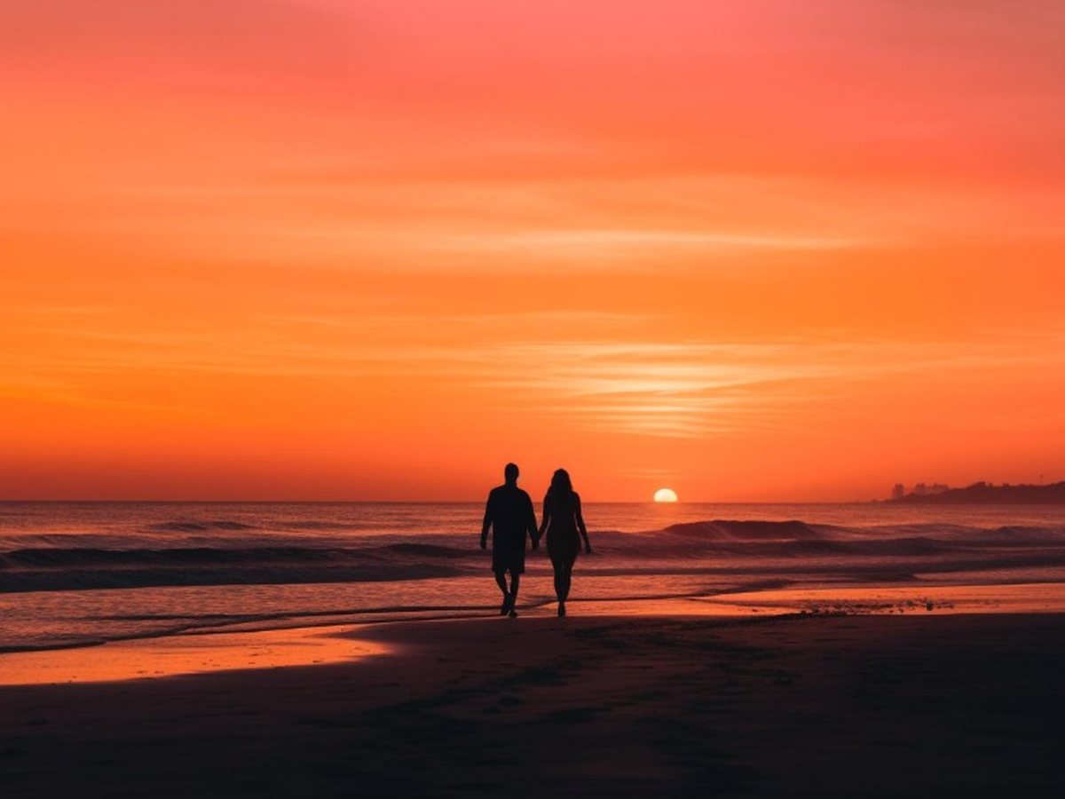 A couple walking together on a beach at sunset